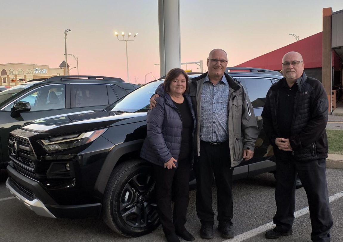 Deux hommes et une femme sont debout devant une voiture Toyota