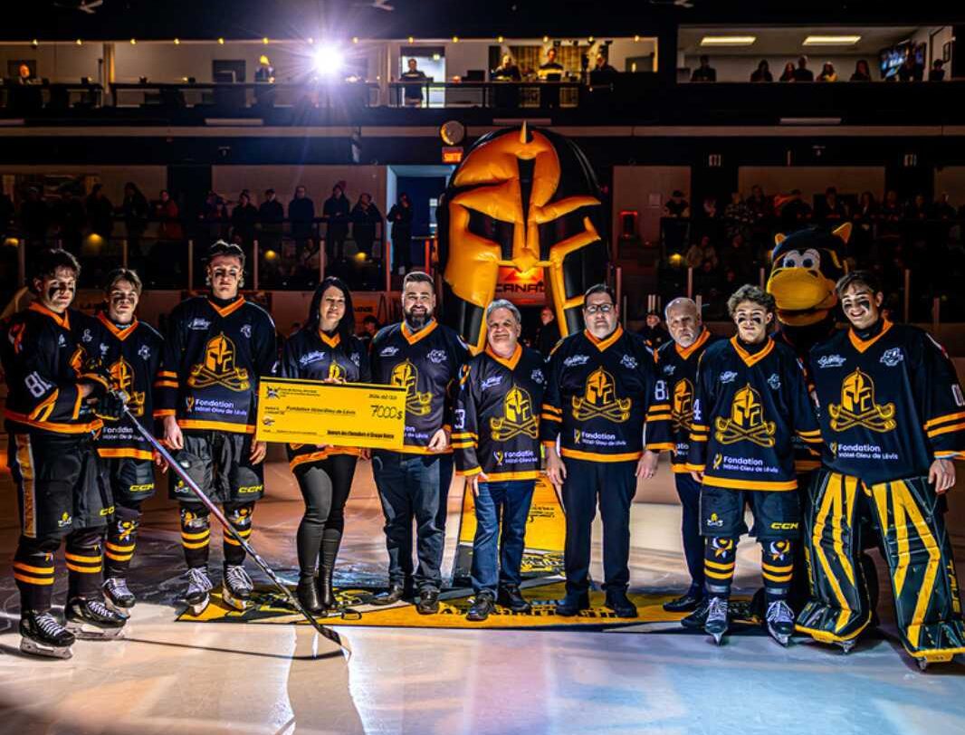 Des joueurs de hockey des Chevaliers de LÉvis habillés en noir et jaune avec un chèque donnant 7000$ à la Fondation Hôtel-Dieu de Lévis.