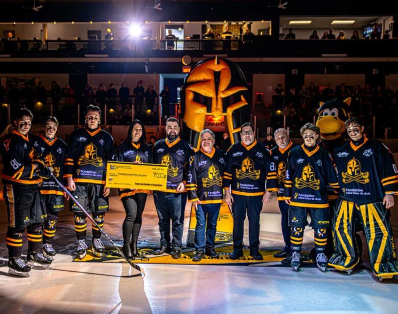 Des joueurs de hockey des Chevaliers de LÉvis habillés en noir et jaune avec un chèque donnant 7000$ à la Fondation Hôtel-Dieu de Lévis.